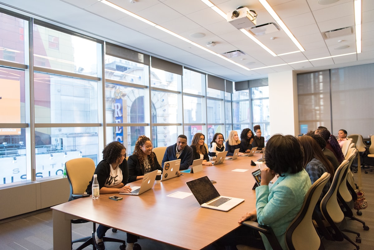 A large diverse team seated around a long conference table with laptops